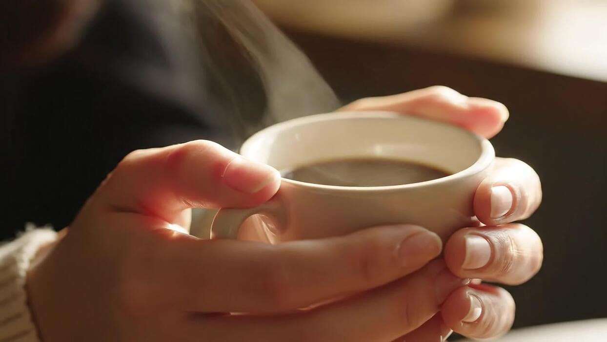 Hands cupped around a warm ceramic mug, steam rising in soft light